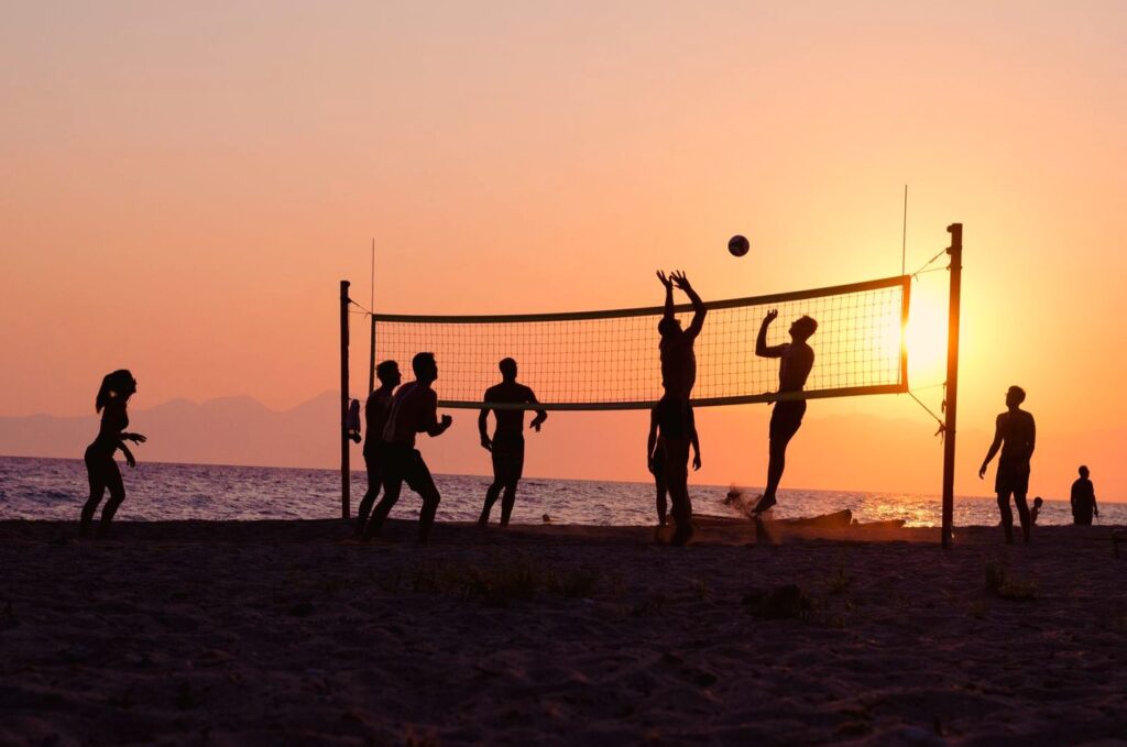 Silhuetter af mennesker, der spiller beachvolleyball ved solnedgang